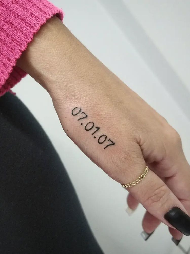 Mão de pele clara com tatuagem "07.01.07" no dedão