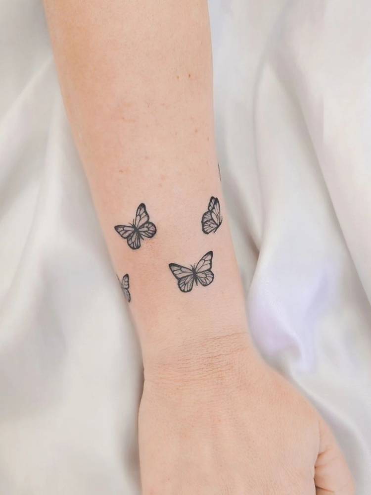traco-fino-delicada-borboleta Tatuagem de borboletas pequenas em traço fino no pulso, formando uma espécie de bracelete. Foi feita numa mulher de pele clara.